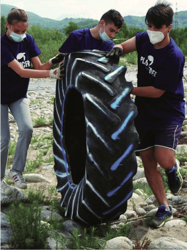 Three individuals wearing plastic free shirts are carefully grasping a sizable tire